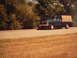 1977 Ford F-150 - A blue 1977 Ford F-150 flatbed truck is seen driving on a road with trees in the background.
