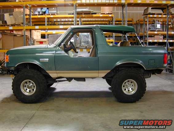 Green Ford Bronco with lifted suspension and large tires, viewed from the side