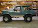 1989 Ford Bronco - A green Ford Bronco with a lifted suspension and large off-road tires is parked indoors.
