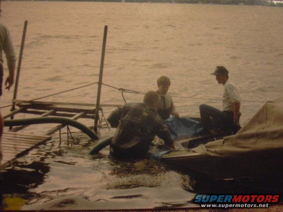 Boat partially submerged in water with three people and a tarp