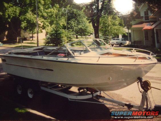 White boat on a dual-axle trailer parked on a street, with houses and trees in the background