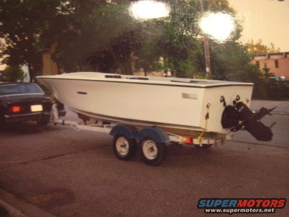 Black car towing a white boat on a dual-axle trailer down a street