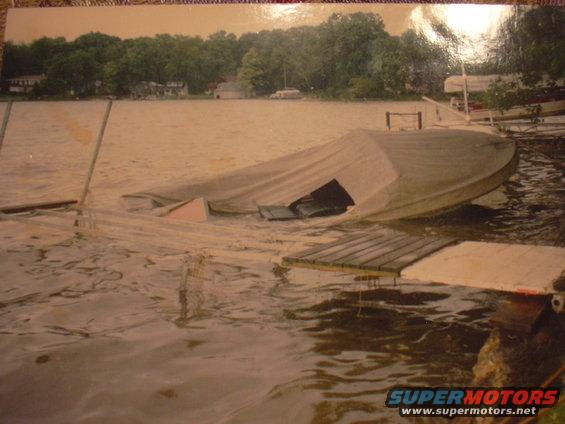 Boat covered by a tarp, partially sunk in the water next to a dock