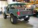 1989 Ford Bronco - Modified 1989 Ford Bronco seen from the rear in a workshop setting. It has large off-road tires and a custom bumper.