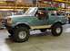 1989 Ford Bronco - This lifted Ford Bronco is parked inside a warehouse with storage shelves visible in the background.