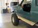1989 Ford Bronco - Side view of a green 1989 Ford Bronco, a large off-road tire and tan lower body trim.