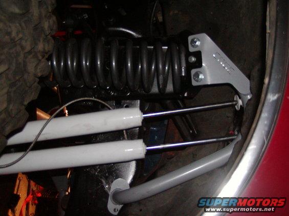 Close-up of suspension components including a coil spring and two shock absorbers, with a silver bracket labeled 'EDGE'
