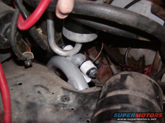 Engine bay with gray and silver hoses, red wire loom, and black hoses. A hand is visible