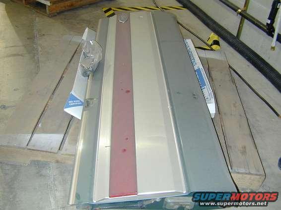 Silver car hood panel with a red stripe down the center, resting on wooden planks