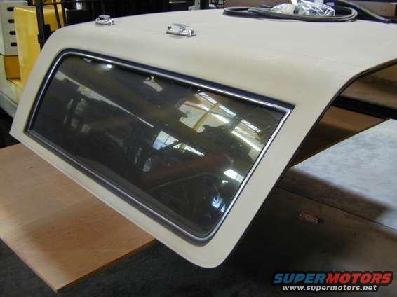 Vehicle hardtop with a side window, resting on a wooden surface. A yellow forklift is visible in the background