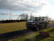 1992 Ford Bronco - A black 1992 Ford Bronco is shown driving on a paved path with a field and power lines in the background.