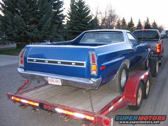 Blue 1976 Ford Ranchero on a red trailer, being towed by a pickup truck