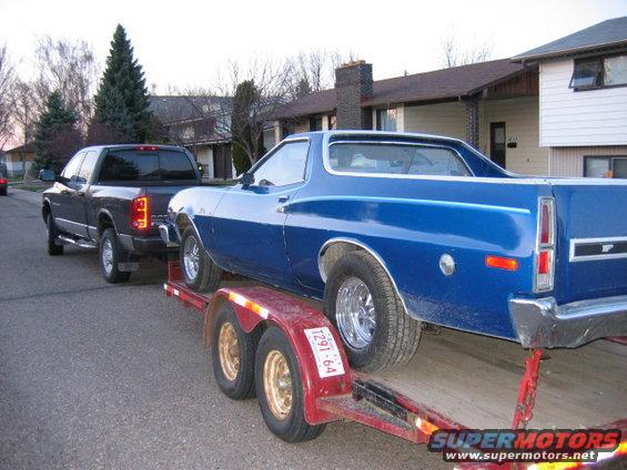 Blue coupe utility being towed on a trailer by a dark pickup truck
