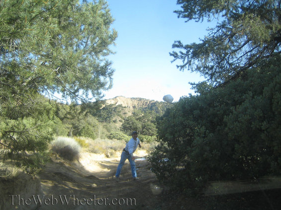 Person throwing a rock in a dry, hilly landscape with trees and bushes