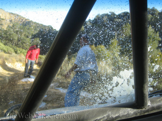 Off-road vehicle interior view of two people in a dusty, watery outdoor environment