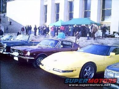 Yellow Chevrolet Corvette C4 parked in front of a building with a crowd and other classic cars
