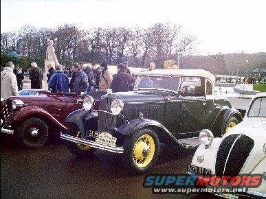 Dark green convertible with yellow wheels and a white top, parked next to a maroon car and a white car
