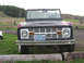 1968 Ford Bronco - A classic 1968 Ford Bronco is parked outdoors, facing the camera with a view of a grassy field and trees in the background.