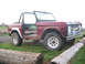 1968 Ford Bronco - A red 1968 Ford Bronco, missing its doors, sits on a grassy field with logs nearby.