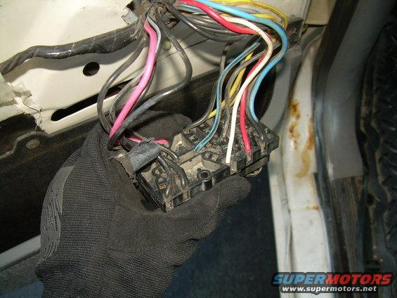 Gloved hand holding a fuse box with many colored wires connected