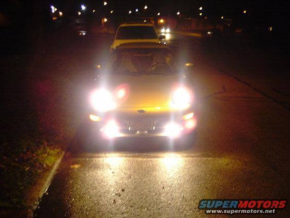Yellow car's headlights on at night, another car behind it
