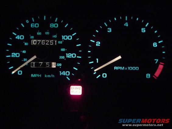 Car dashboard with speedometer showing 75 MPH and tachometer at 1000 RPM. Odometer reads 076251. Brake light is illuminated