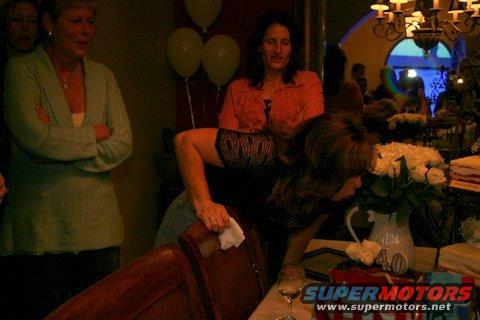 People gathered around a table with a cake and flowers at a party