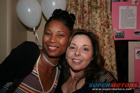 Two women smiling at a party with balloons and a Rolling Stones poster in the background
