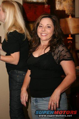 Two women in black tops and jeans at a party. One woman in the foreground is smiling