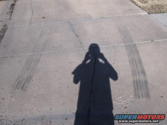 Shadow of person holding camera, tire marks on concrete driveway