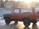 1984 Ford Bronco II - The sun glints off the side of a red 1984 Ford Bronco II, parked in front of a suburban house.