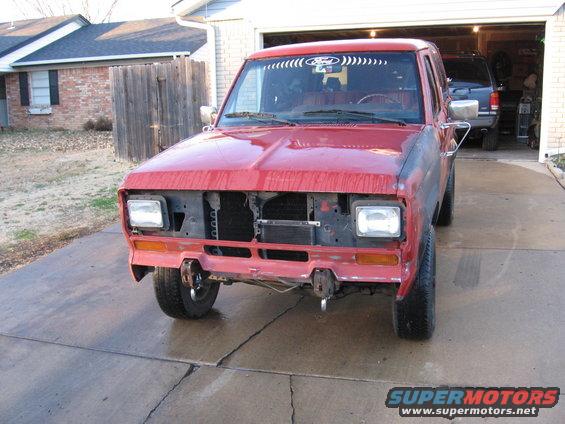 Red 1984 Ford Bronco II with missing grille and front bumper, parked in a driveway
