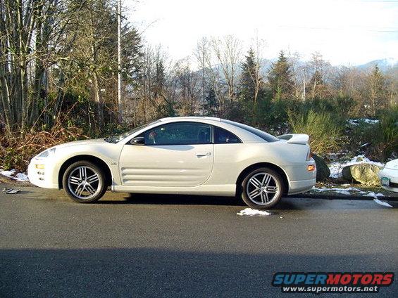 White coupe parked on the side of the road, trees and mountains in the background