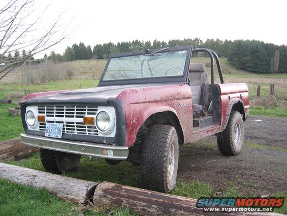 Red 1968 Ford Bronco parked on dirt with logs in front