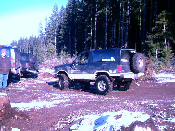 Dark blue 1987 Ford Bronco II with a spare tire mounted on the rear, parked in a snowy, wooded area