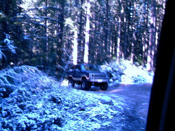 1987 Ford Bronco II on a dirt road covered in snow, surrounded by pine trees