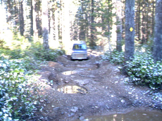 Blue SUV on a muddy, wooded trail with puddles