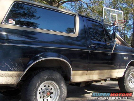 Black and tan 1991 Ford Bronco side view with tinted windows and a basketball hoop in the background