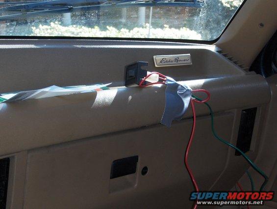 Tan dashboard with an Eddie Bauer badge, wires, and papers. Sunlight streams through the windshield