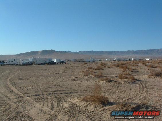 desert landscape with many RVs and trucks parked in rows under a clear blue sky
