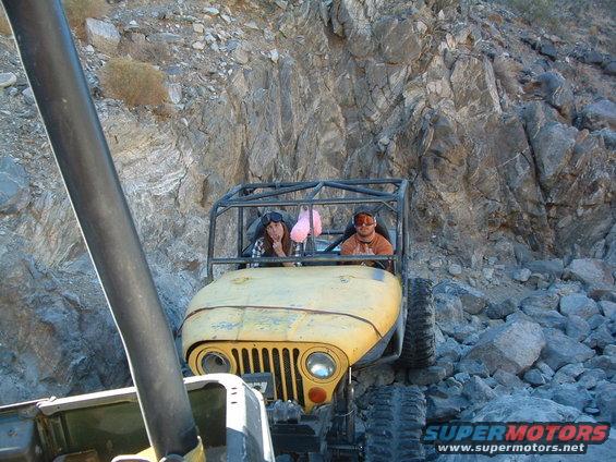 Yellow Jeep with roll cage driving on rocky terrain. Two people inside