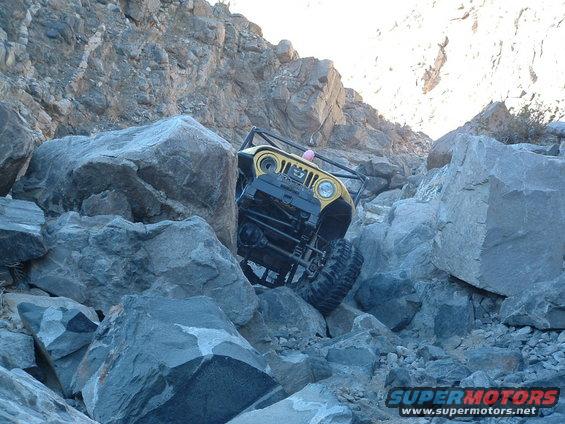 Yellow 1994 Jeep YJ navigating a steep, rocky trail with its front wheels angled up