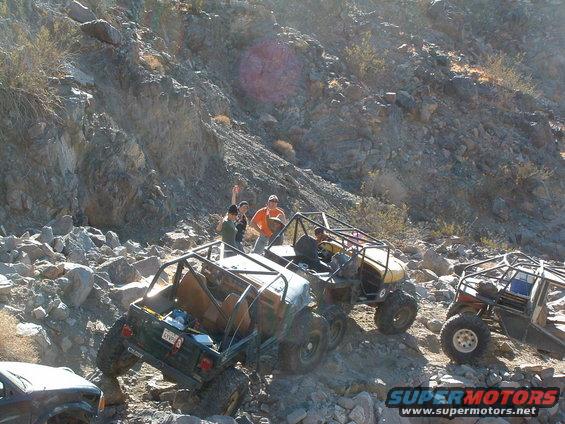 Several off-road vehicles navigating a steep, rocky slope with people watching