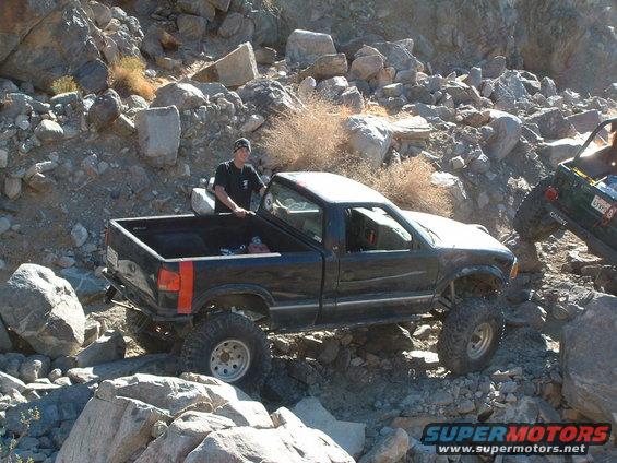 Black pickup truck with lifted suspension and off-road tires navigating rocky terrain