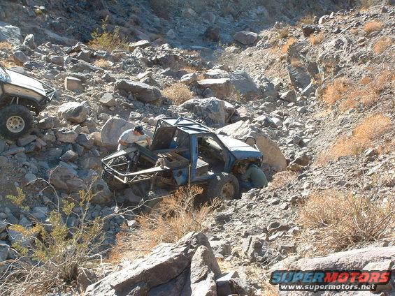 Off-road buggy with roll cage navigating a rocky slope, another vehicle visible on the left