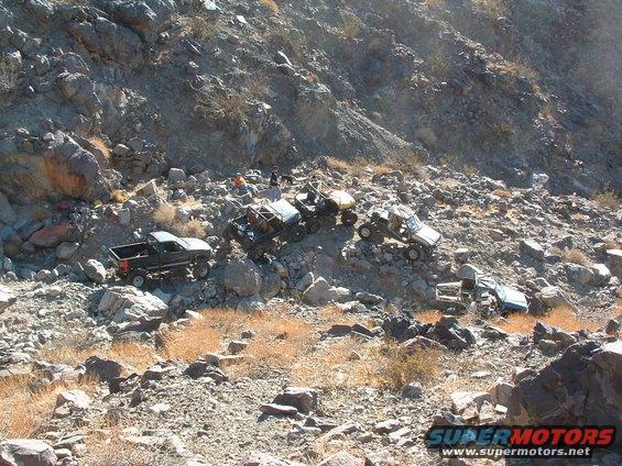 Several off-road vehicles navigating a steep, rocky slope with sparse vegetation