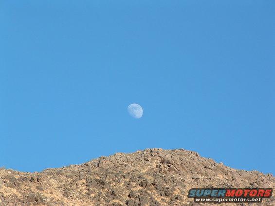 Moon in blue sky over rocky hill with SuperMotors logo