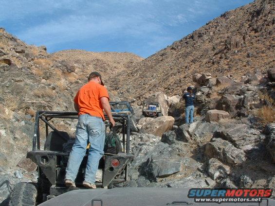 Two off-road vehicles on a rocky mountain trail with people standing near them