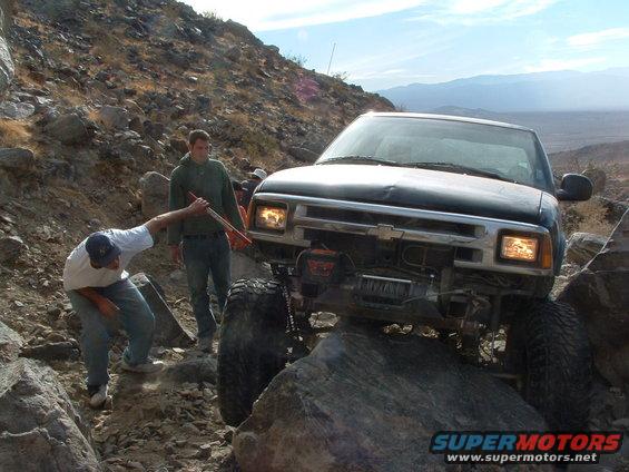 Black Chevrolet S-10 pickup truck on rocky terrain with two people assisting