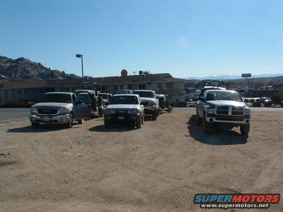 Several pickup trucks parked on a dirt lot in front of a motel, one towing a trailer
